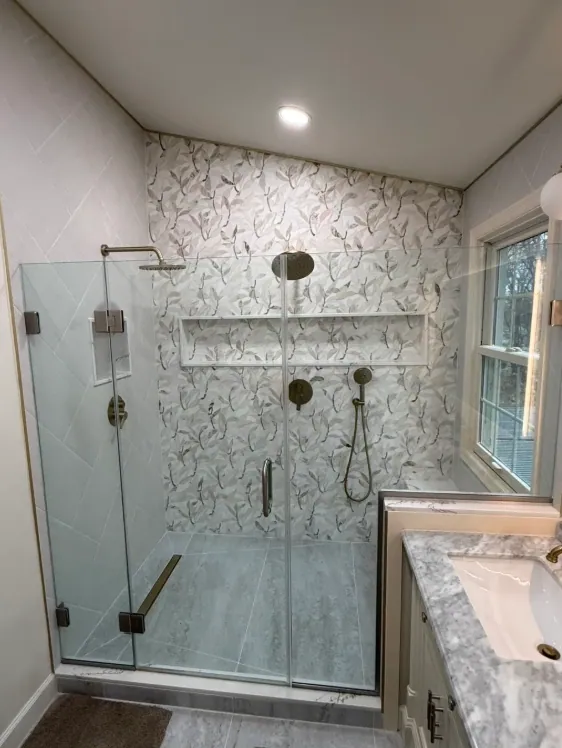Walk-in shower with a leaf-pattern tile wall, long niche, linear drain and brushed brass fixtures