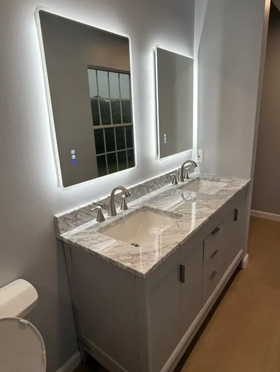 Double vanity with a marble-look top, two backlit mirrors and brushed nickel faucets