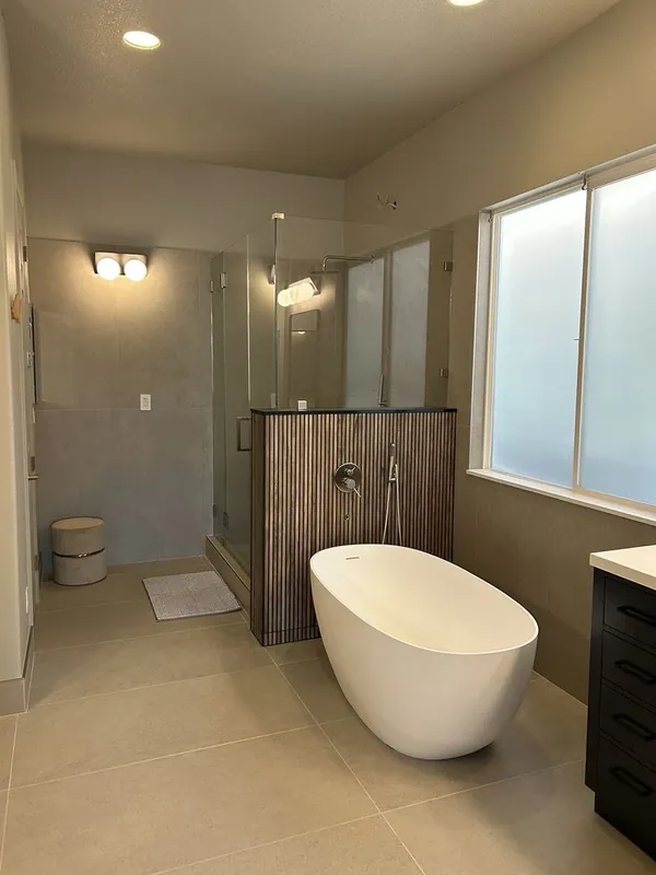Freestanding tub in front of a fluted half wall with a wall-mounted tub filler, glass shower behind