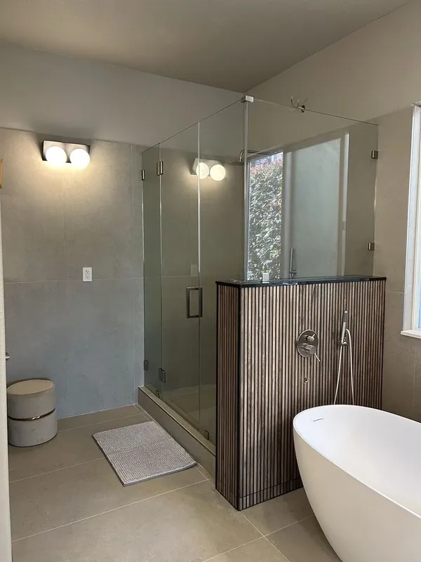 Frameless glass shower above a fluted half wall, large gray wall tile behind