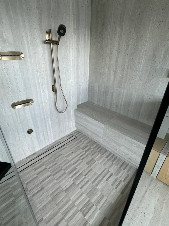 Gray stone-look shower with a long tiled bench, strip mosaic floor and linear drain