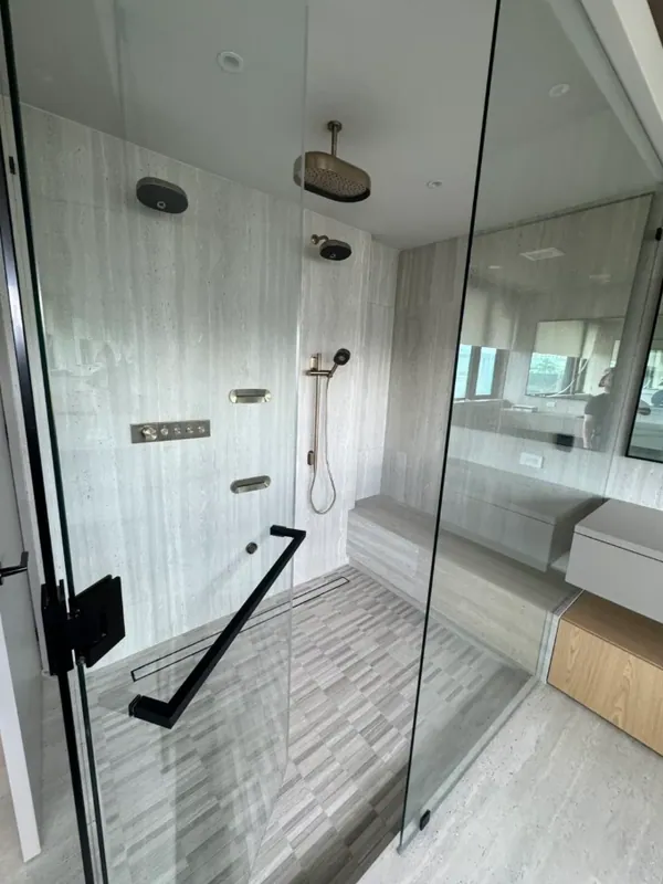 View through the glass of the gray shower with a ceiling rain head and brushed brass fixtures