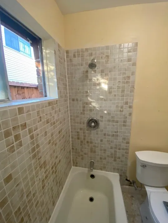 Mosaic tub wall with chrome shower head and valve, window to the left