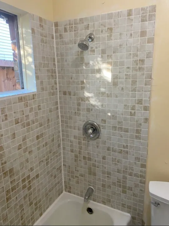 Shower head wall of the beige mosaic tub surround