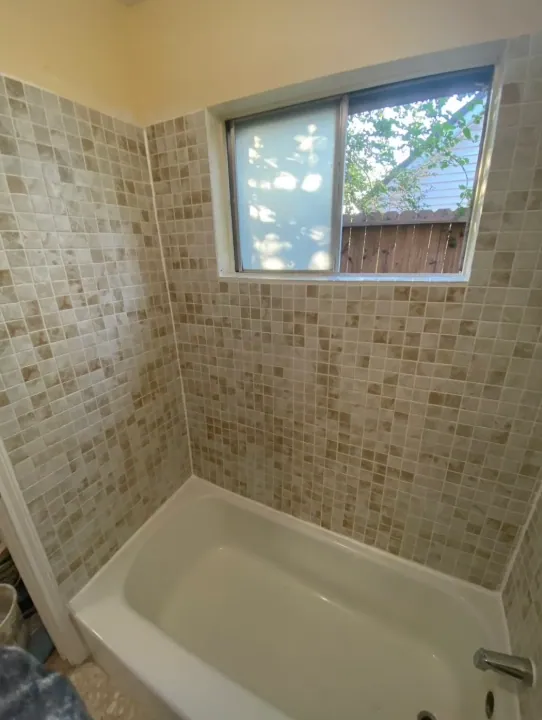 Back and side walls of the beige mosaic tub surround around the window
