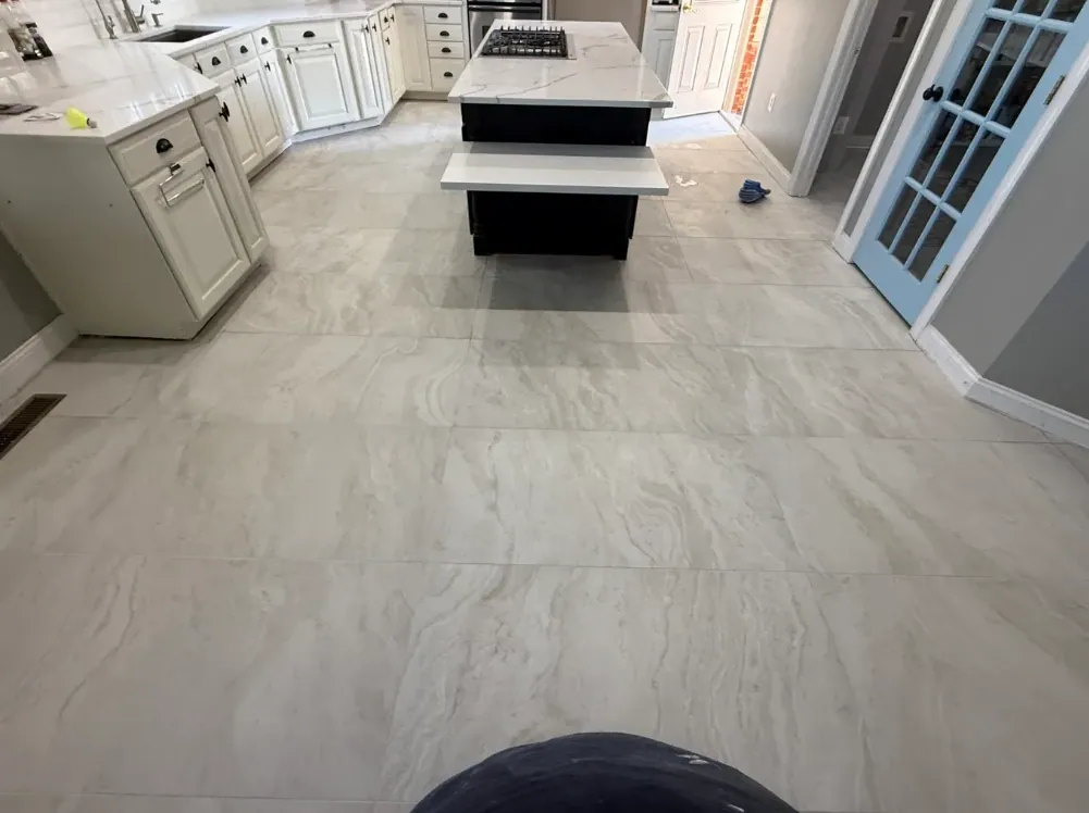 Kitchen floor of large light-gray veined tiles running toward the island