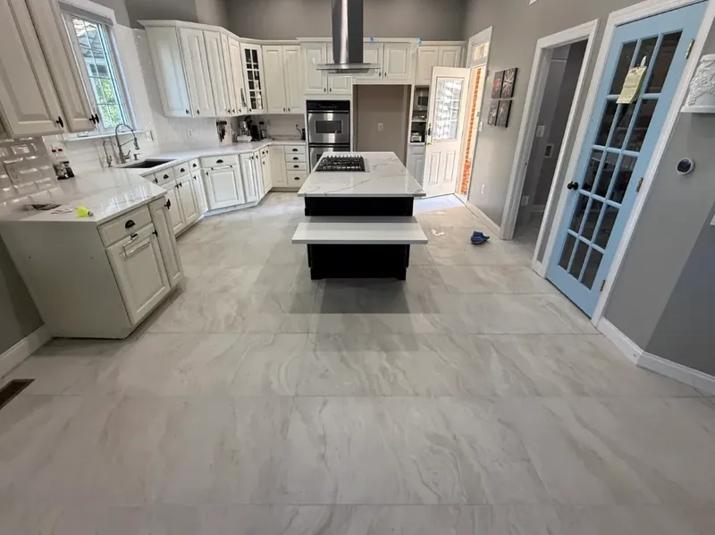 Wide view of the kitchen with large light floor tile around the island and cabinets