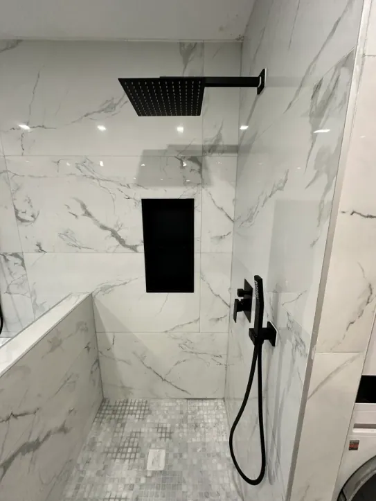Walk-in shower with white marble-look walls, black rain head and niche, and a square mosaic floor