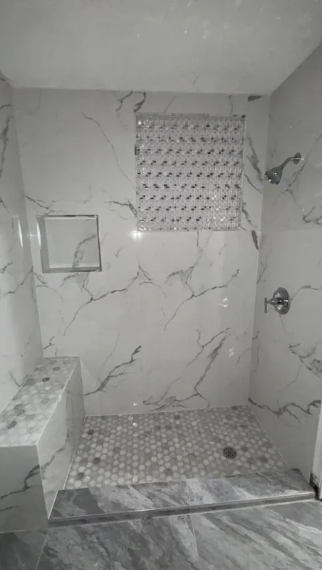 Walk-in shower with white marble-look walls, a decorative mosaic panel, niche, bench and hex mosaic floor