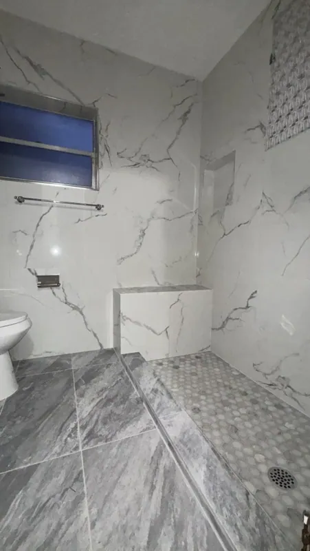 Shower bench and hex mosaic floor beside the gray diagonal bathroom floor
