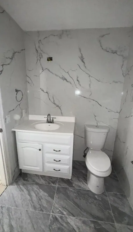 Vanity and toilet against white marble-look walls on a dark gray tile floor