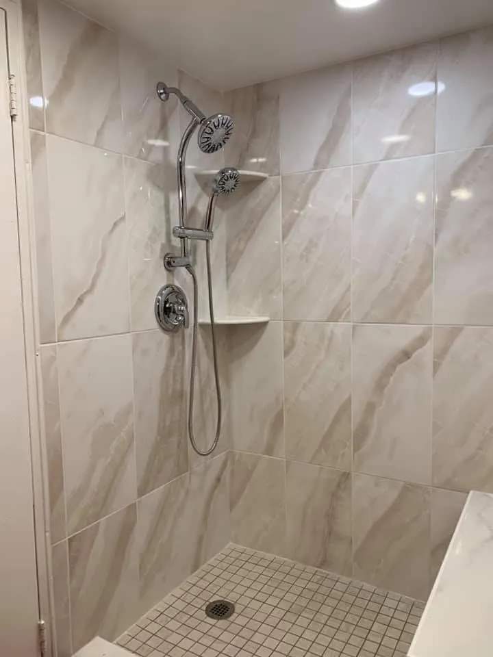Light marble-look tiled shower with dual showerhead and small square mosaic floor