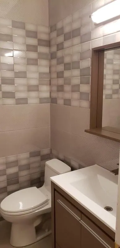 Separate bathroom with gray and white block-pattern wall tile, toilet and vanity