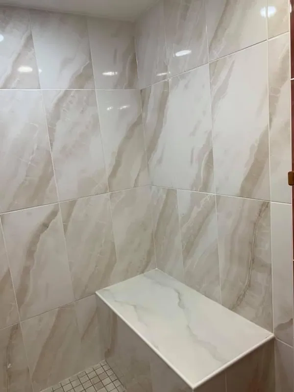 Built-in shower bench surrounded by light marble-look wall tile
