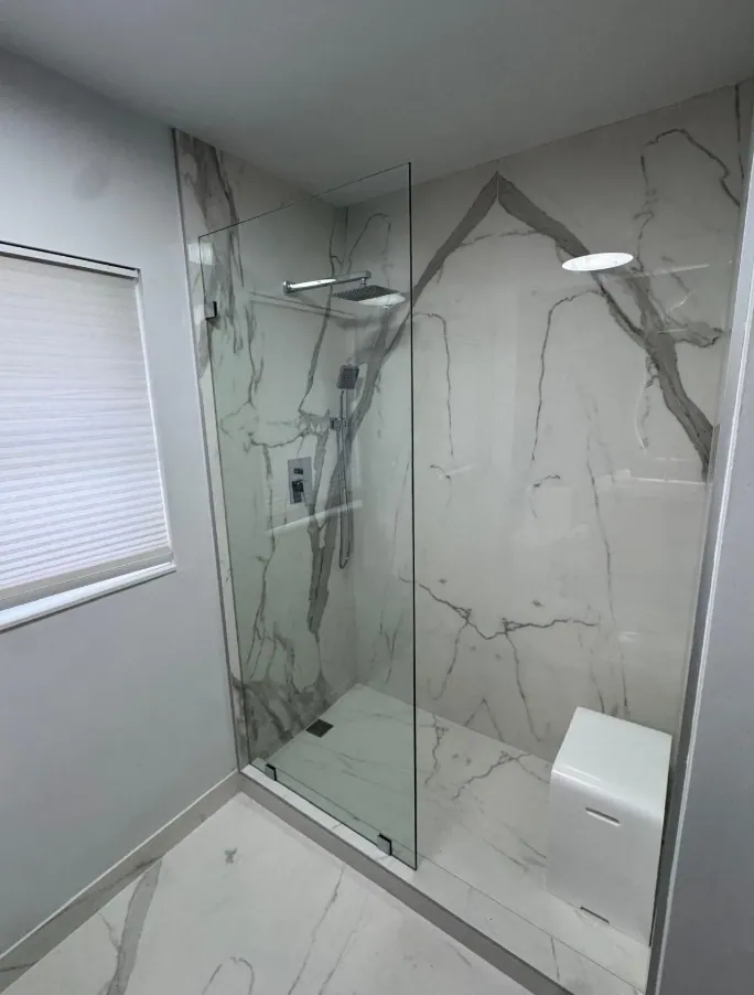 Walk-in shower with a fixed glass panel and large white marble-look tiles with bold gray veins
