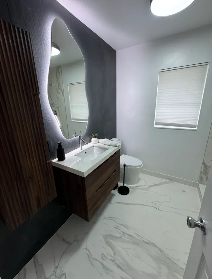 Floating wood vanity with a backlit mirror, fluted wood panel and white marble-look floor tile