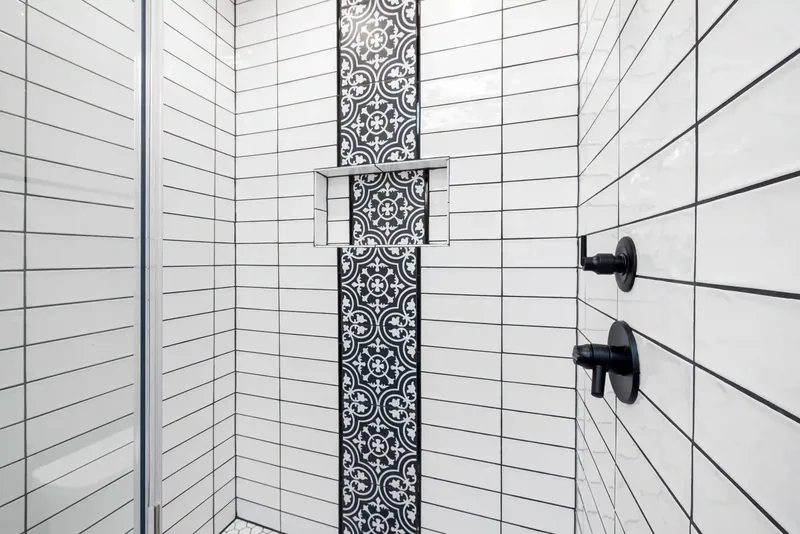 White rectangular tiled shower with a dark patterned vertical accent and black fixtures
