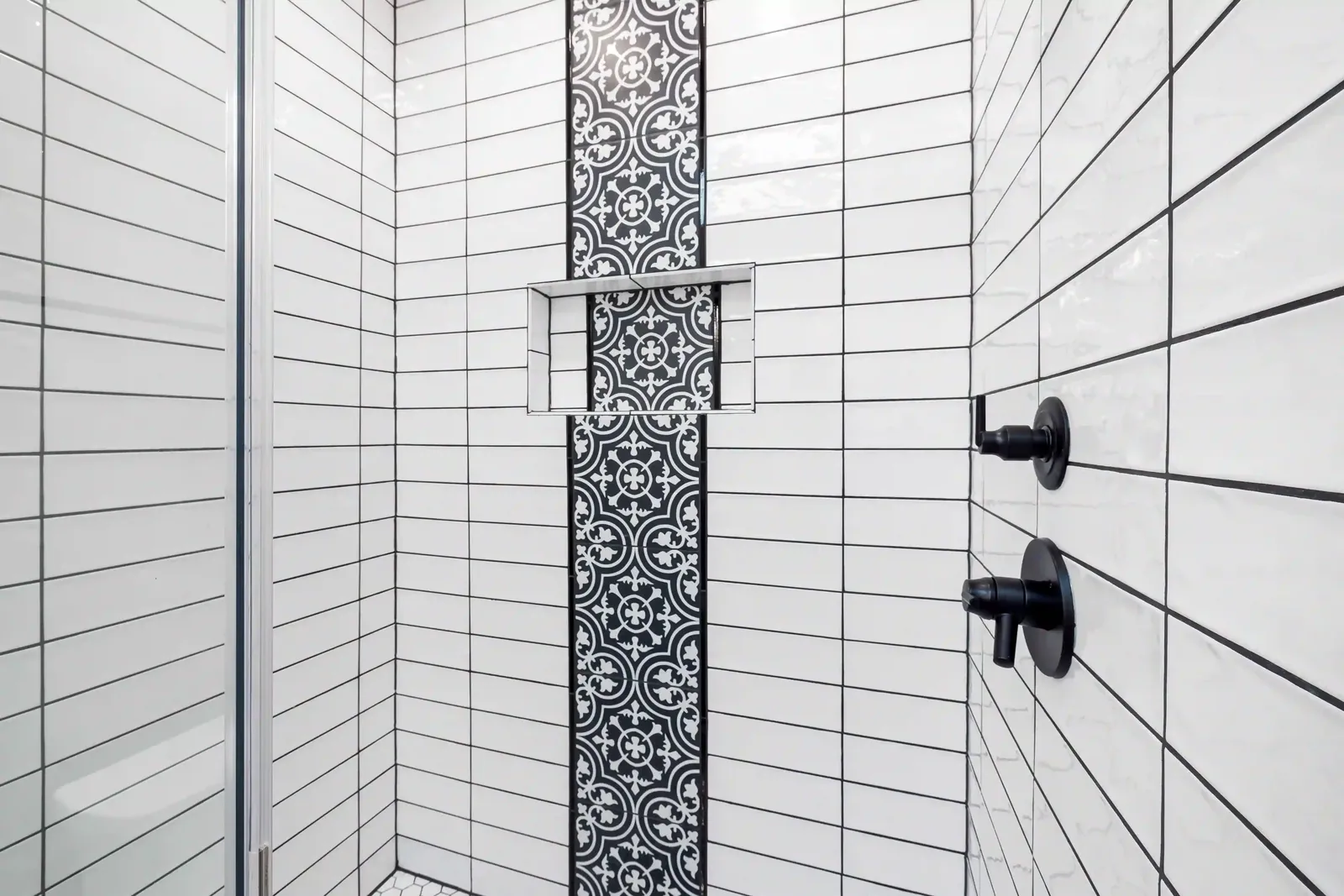 White rectangular tiled shower with a dark patterned vertical accent and black fixtures